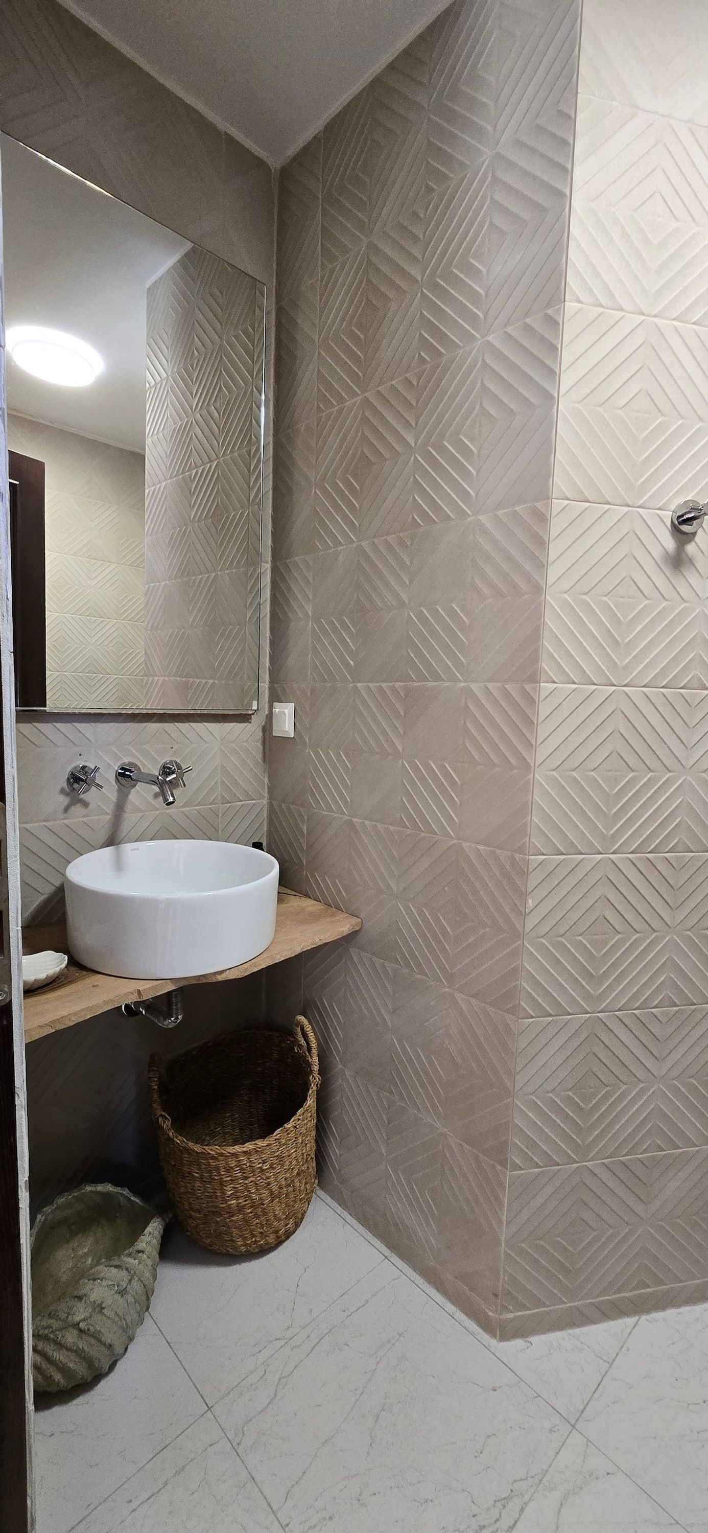 A bathroom with a round sink, a mirror, and patterned wall tiles.