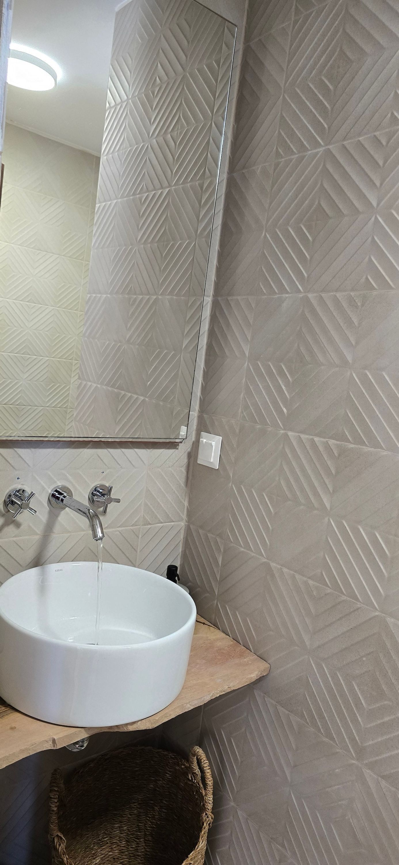 A bathroom with a white sink, a mirror, and a textured wall.