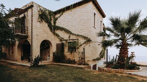 A stone building with arched doorways, ivy-covered walls, and a palm tree in the foreground. - Luxury Villa Rodianna (Malevizi)