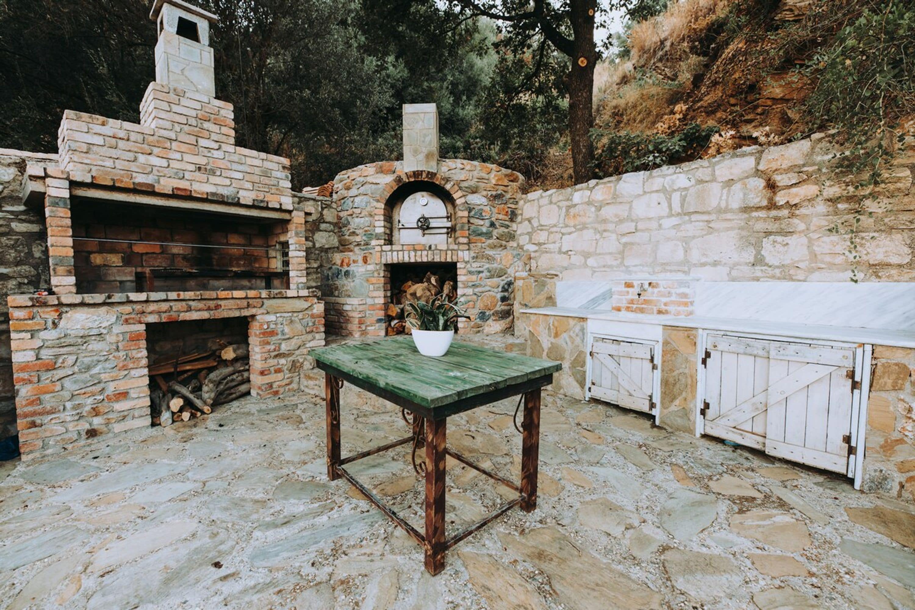 Une terrasse extérieure avec un four en briques, un mur en pierre et une table en bois.