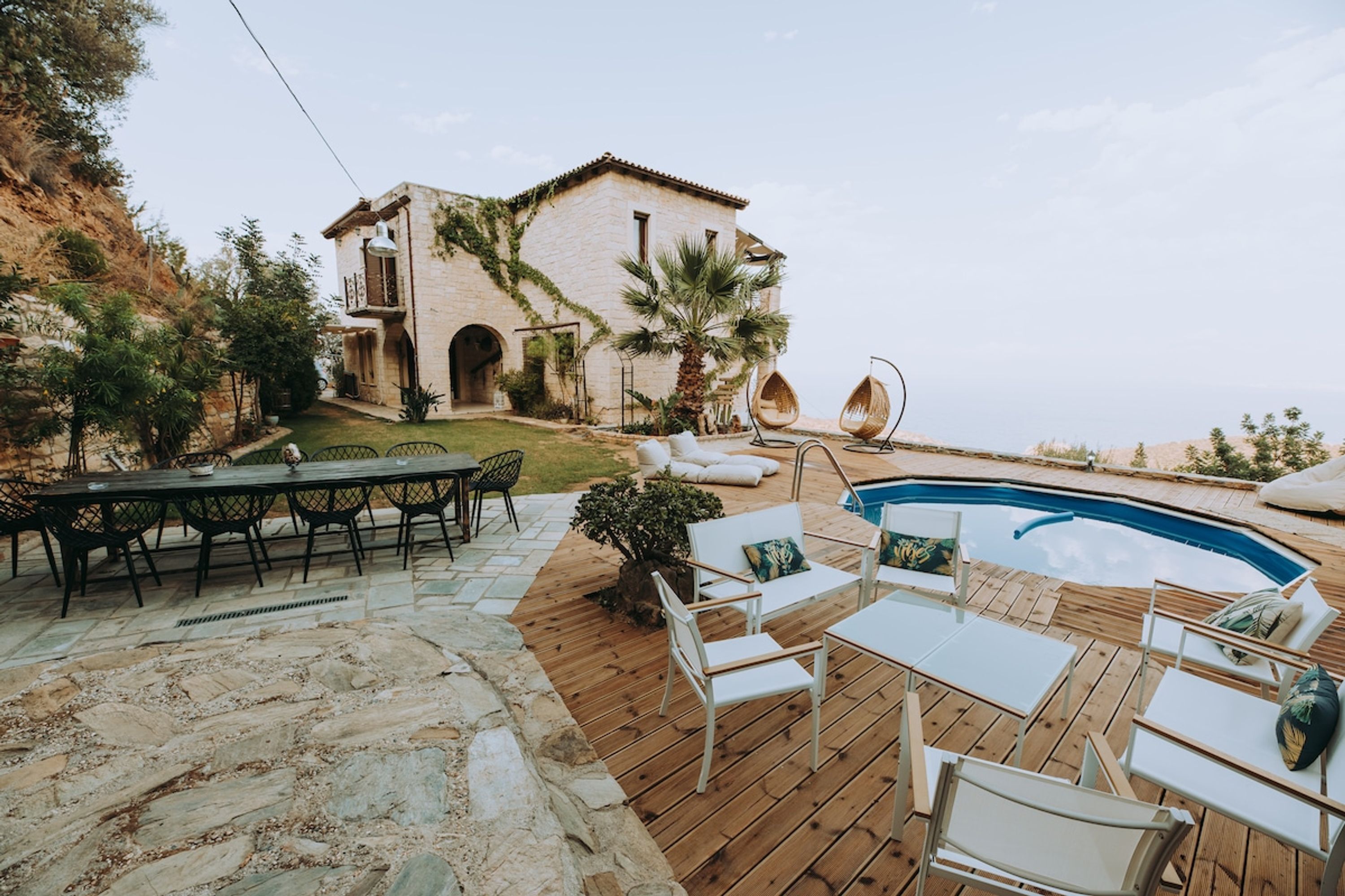 A poolside area with a stone deck, white lounge chairs, and a dining table with chairs.