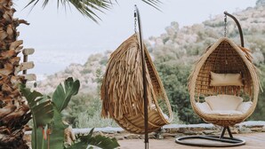 Two wicker hanging chairs with cushions, placed on a wooden deck with a view of a mountainous landscape. - Luxury Villa Rodianna (Malevizi)