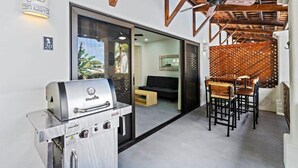 A modern outdoor patio with a built-in grill, a dining area with wooden chairs, and a ceiling fan. - Modern Split-Level 2-Bedroom Condo with Pools, Terrace & Easy Beach Access (Sardinal)