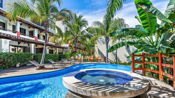 A pool area with lounge chairs, a hot tub, and palm trees. - Modern Split-Level 2-Bedroom Condo with Pools, Terrace & Easy Beach Access (Sardinal)