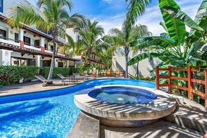 A pool area with lounge chairs, a hot tub, and palm trees. - Modern Split-Level 2-Bedroom Condo with Pools, Terrace & Easy Beach Access (Sardinal)