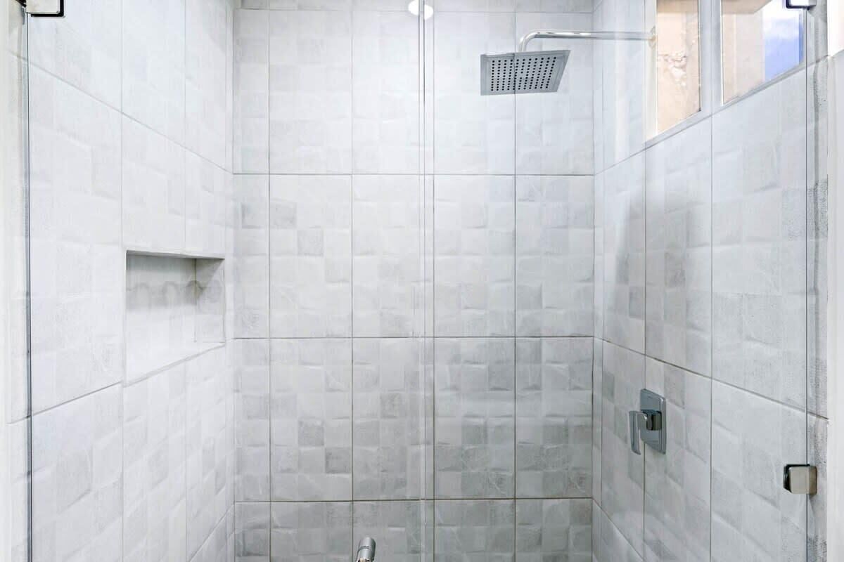 Un área de ducha moderna con puerta de cristal, alcachofa y panel de control.