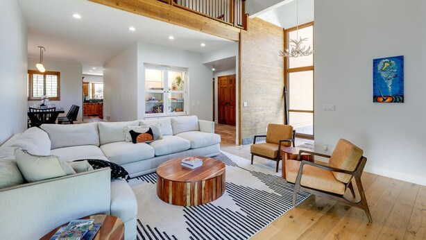 A spacious living room with a high ceiling, a wooden staircase, and a dining area with a view of the kitchen.