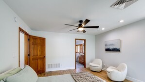 A bedroom with a bed, a ceiling fan, a wooden door, a bathroom visible through an open door, and a wall-mounted picture.