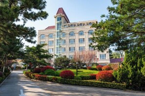 A large building with a prominent tower, surrounded by well-maintained gardens and a clear sky.