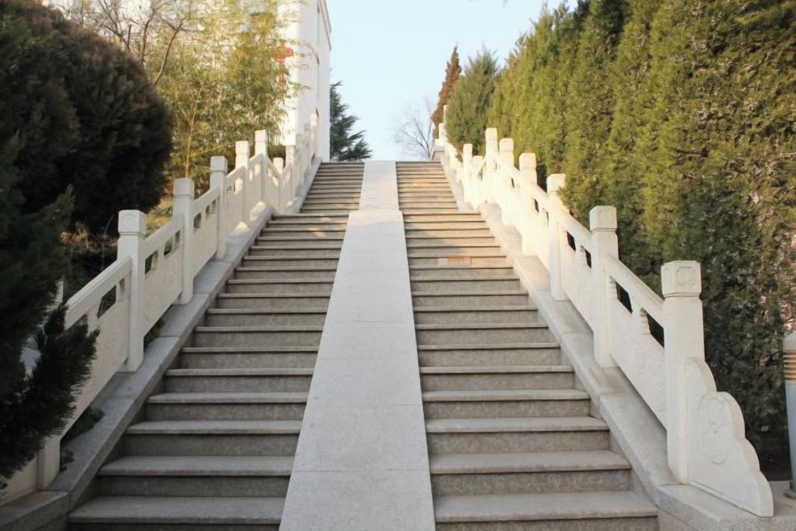 A set of stone steps with white railings, leading up a hill.