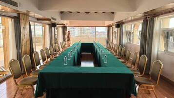 Un salón de conferencias con una larga mesa y sillas, ventanas grandes y vistas a edificios.