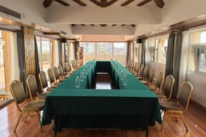 Un salón de conferencias con una larga mesa y sillas, ventanas grandes y vistas a edificios.