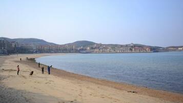 A beach with people walking along the shore, a calm sea, and buildings in the background.