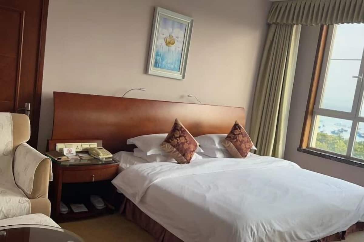A hotel room with a large bed, a nightstand with a telephone, a chair, and a window with curtains.