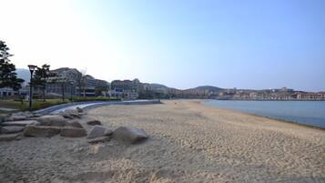 A beach with a clear sky, a sandy shore, and buildings in the background.