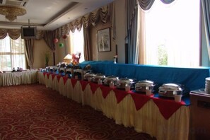 A banquet hall with a long table covered with a blue cloth, lined with silver serving dishes, and a carpeted floor.