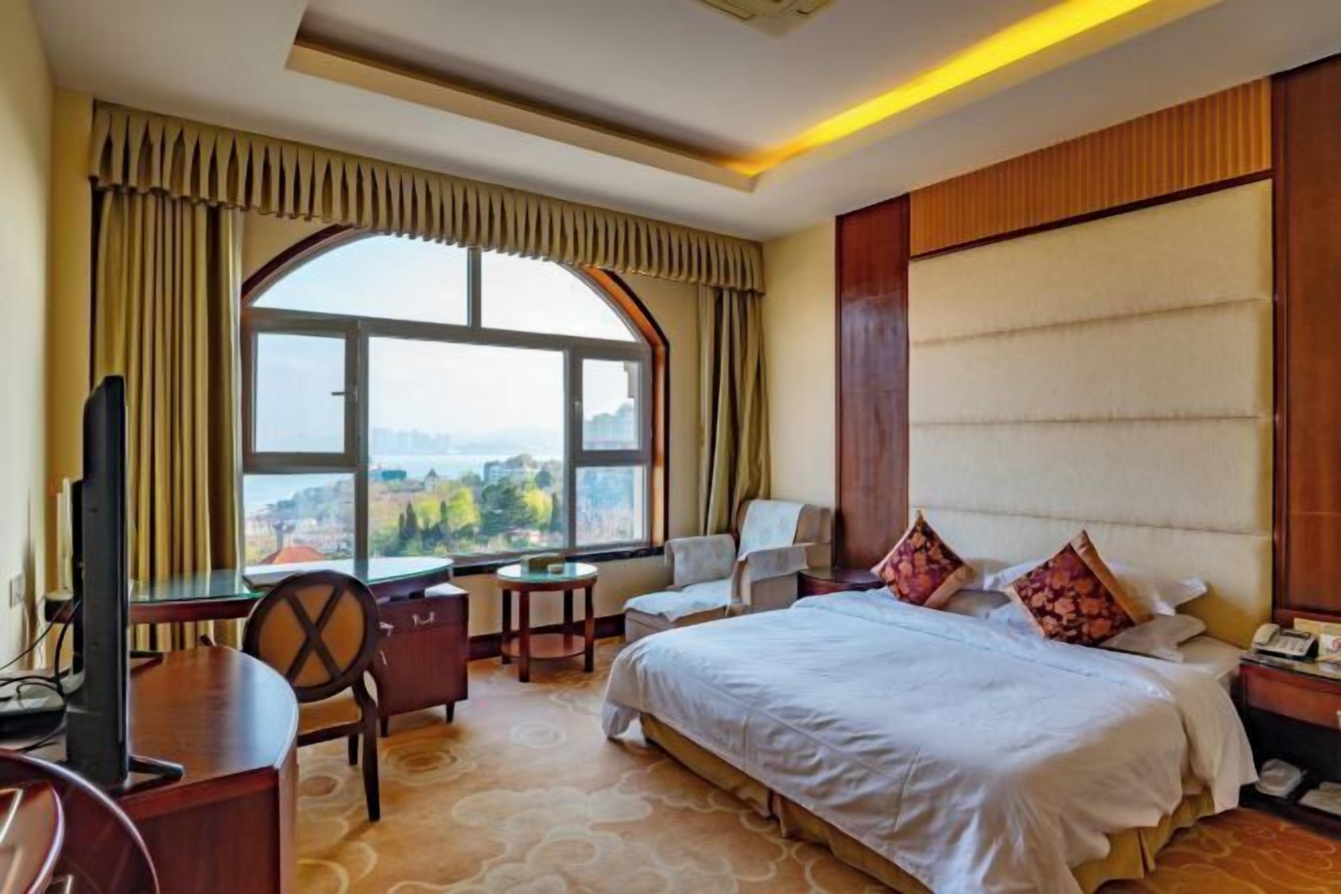 Quarto de hotel com uma cama grande, uma escrivaninha, uma cadeira, uma televisão e vista para a cidade.