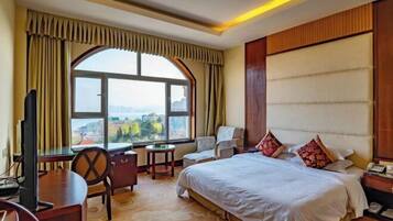 Quarto de hotel com uma cama grande, uma escrivaninha, uma cadeira, uma televisão e vista para a cidade.