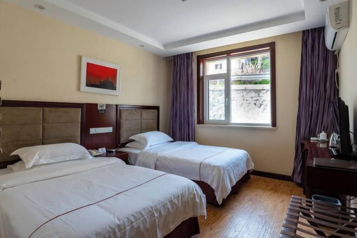 A hotel room with two beds, a desk, a chair, a window with curtains, and a picture on the wall.