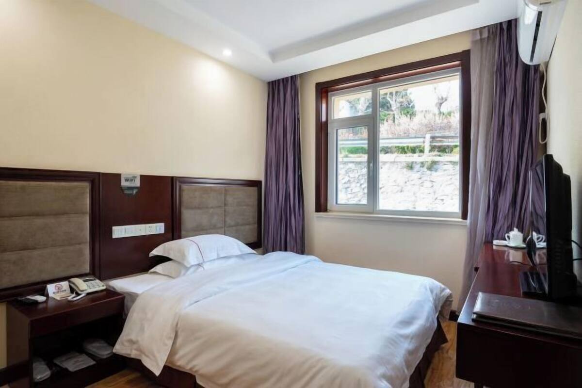 A hotel room with a bed, a desk with a computer, a telephone, and a window with curtains.