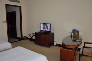 Habitación de hotel con televisión sobre un mueble de madera, una mesa redonda y dos camas.