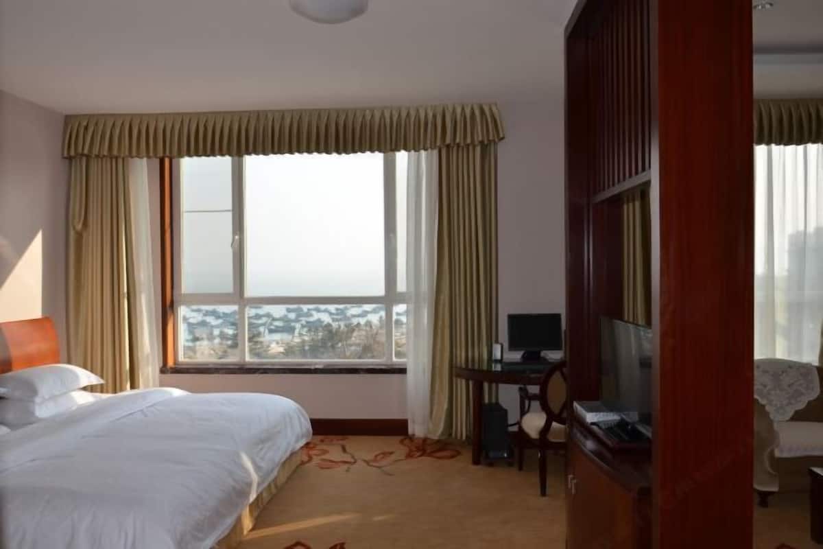 A hotel room with a bed, a desk with a computer, a TV, and a view of a cityscape through the window.