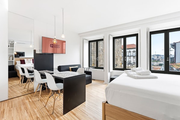 Ein modernes Hotelzimmer mit Bett, Essbereich und großen Fenstern mit Blick auf die Stadt.