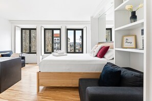 Een moderne slaapkamer met een bed, een bank, een bureau en grote ramen met uitzicht op de stad.
