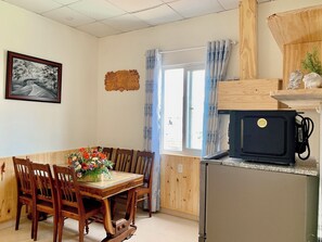 A dining area with a wooden table and chairs, a black refrigerator, and a window with curtains.