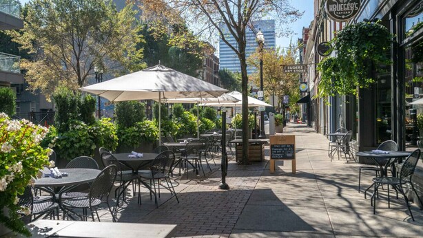 Un café en plein air avec des tables, des chaises, des parasols et un menu écrit à la craie sur un tableau noir.