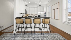 Une cuisine moderne avec des meubles blancs, un îlot central doté de tabourets et des luminaires suspendus.