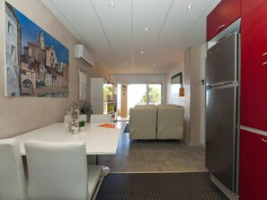 A modern kitchen with a refrigerator, a dining area with a table and chairs, and a view of the outdoors through a glass door. - Apartment in Roses With Sea Views & Pool (Roses)