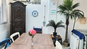 A dining area with a wooden table, chairs, a vase with flowers, a decorative wall clock, and a potted plant.