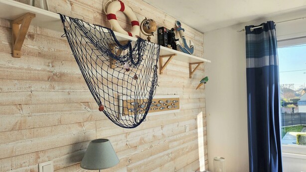 A room with a wooden wall, a hanging net, a globe, and a shelf with nautical decorations.