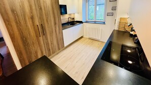 A modern kitchen with wooden cabinets, a black countertop, a window with a view, and a built-in oven. - Charming flat in the heart of Gérardmer (Gérardmer)