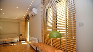 A modern living room with a wooden floor, a sofa, a small table, and a lamp. - Athens top floor stylish 2 min walk to metro Panepistimio (Athina)