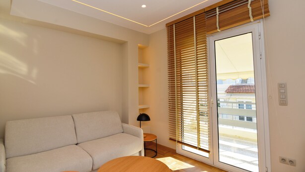 A modern living room with a sofa, a small round table, a lamp, and a sliding glass door with wooden blinds. - Athens top floor stylish 2 min walk to metro Panepistimio (Athina)