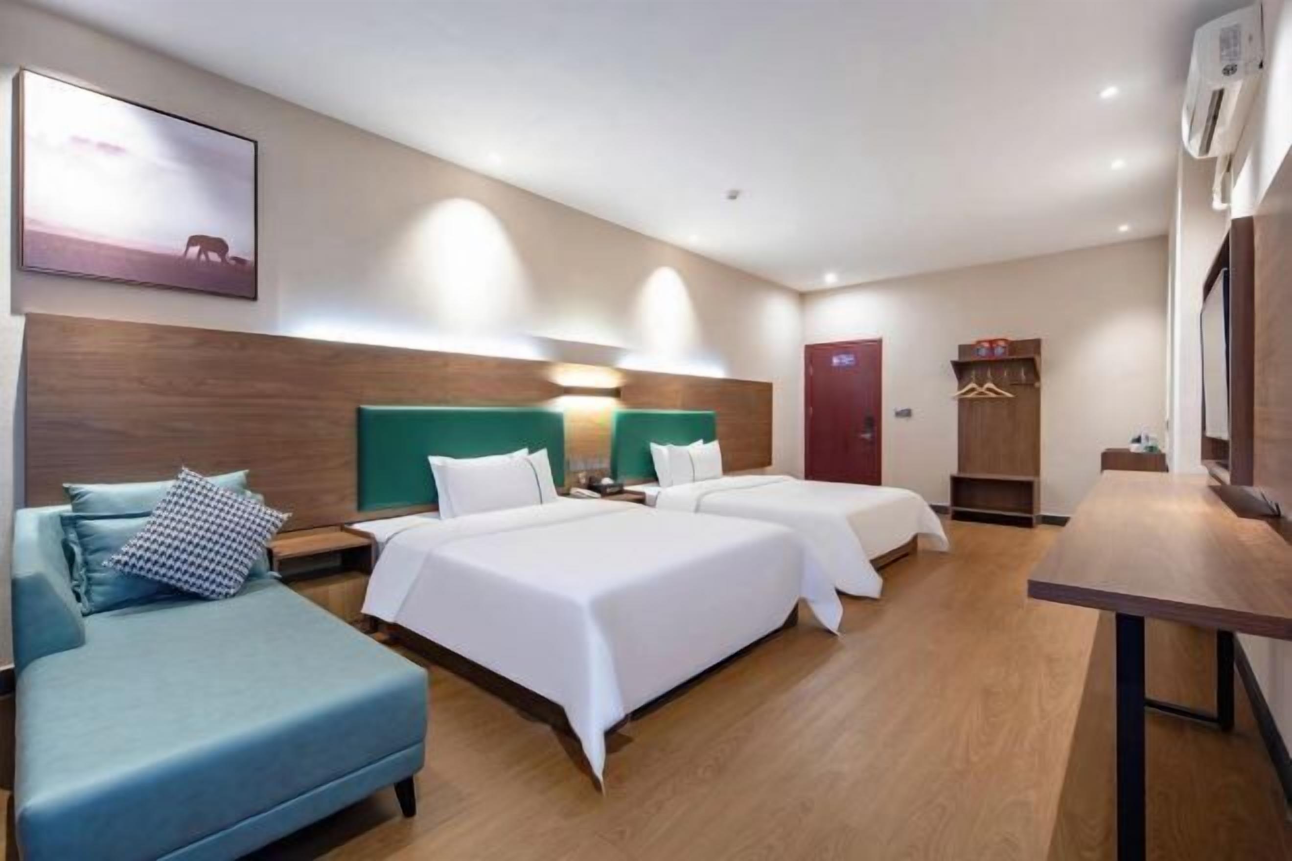 A hotel room with two beds, a sofa, a desk, and a wardrobe.