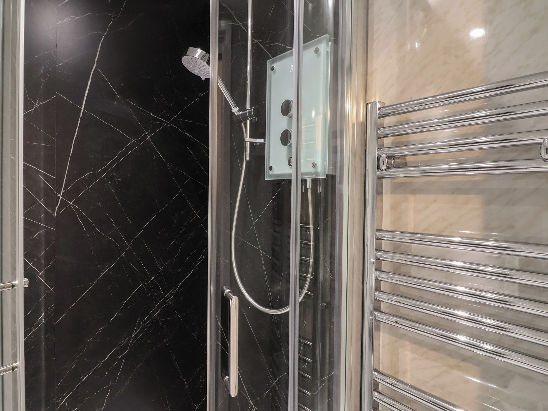 Une douche fermée par des parois en verre, dotée d’un pommeau de douche à main et d’un panneau de commande fixé au mur.