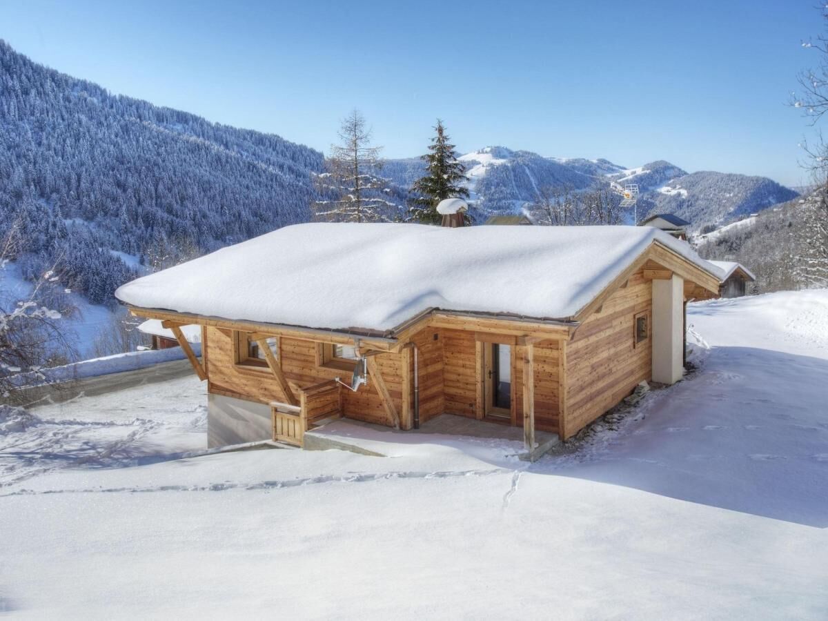Eine Holzhütte mit schneebedecktem Dach, umgeben von verschneiter Landschaft und Bergen.