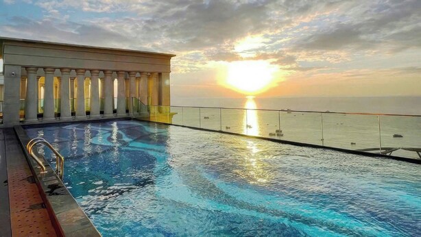 A pool with a sunset view, a covered area with columns, and a clear sky.