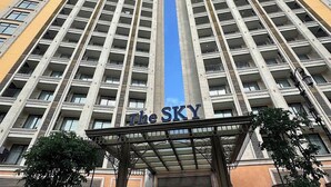 A high-rise hotel with a central entrance, multiple balconies, and a clear sky.
