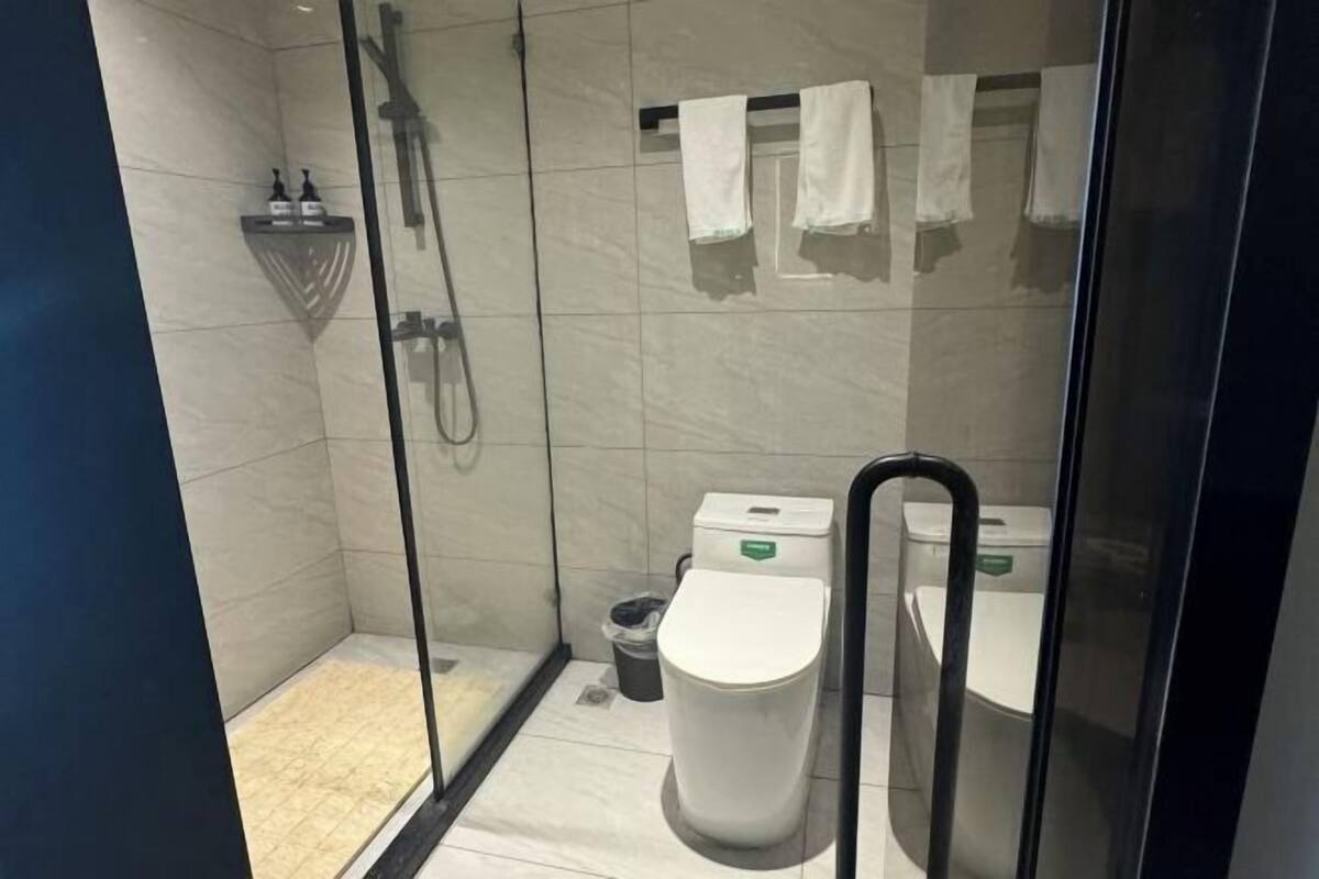 A modern bathroom with a glass shower enclosure, a toilet, and a small trash bin.