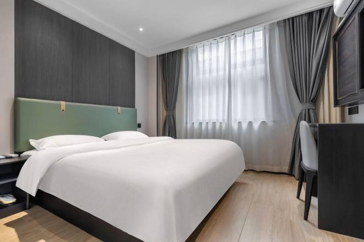 Ein Hotelzimmer mit einem Bett, einem Schreibtisch, einem Stuhl und einem großen Fenster mit Vorhängen.