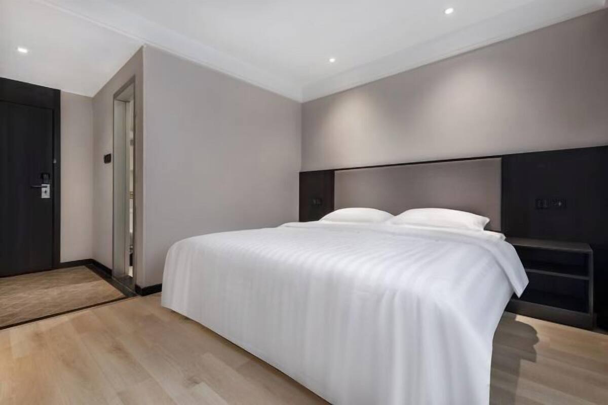 Ein modernes Hotelzimmer mit einem großen Bett, einem dunklen Kopfteil und Holzboden.