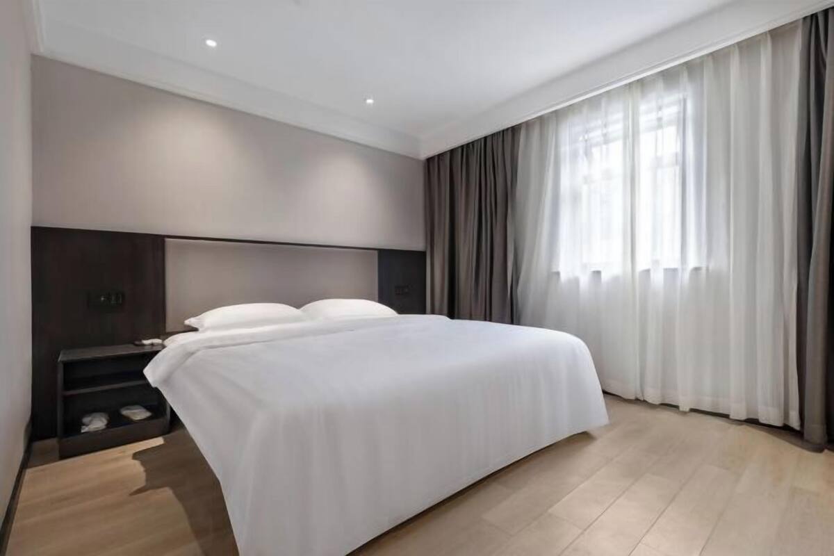Ein modernes Hotelzimmer mit einem großen Bett, einem Nachttisch und einem Fenster mit Vorhängen.