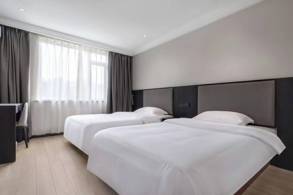 Ein Hotelzimmer mit zwei Betten, einem Schreibtisch und einem Fenster mit Vorhängen.
