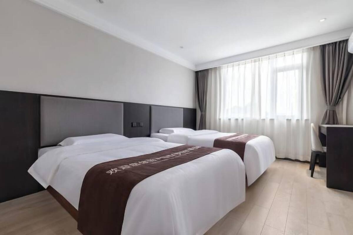 Ein Hotelzimmer mit zwei Betten, einem Schreibtisch und einem großen Fenster mit Vorhängen.