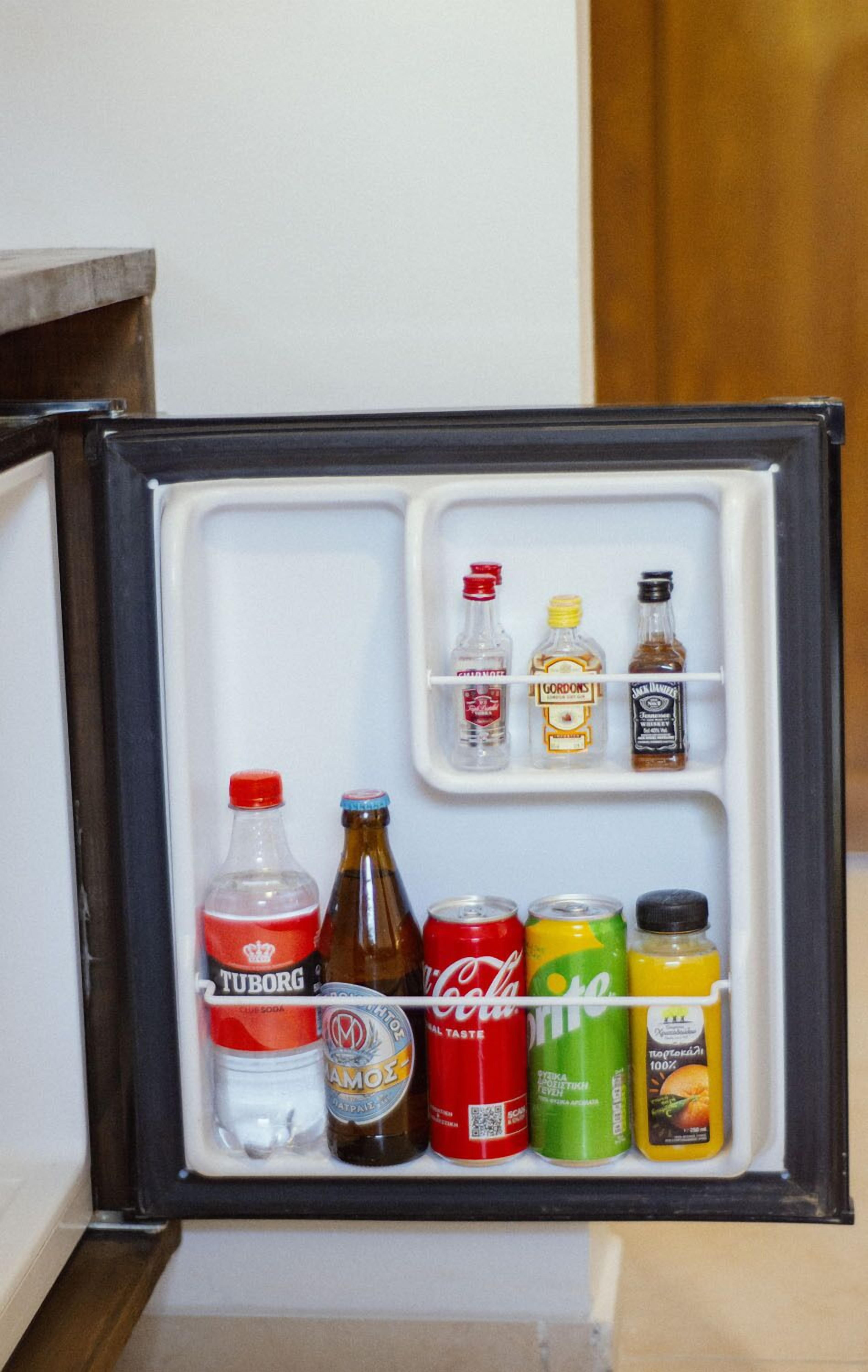 A mini-fridge with various beverages including a bottle of Tuborg, a can of Coca-Cola, a bottle of Jack Daniel's, a can of Sprite, and a bottle of orange juice.