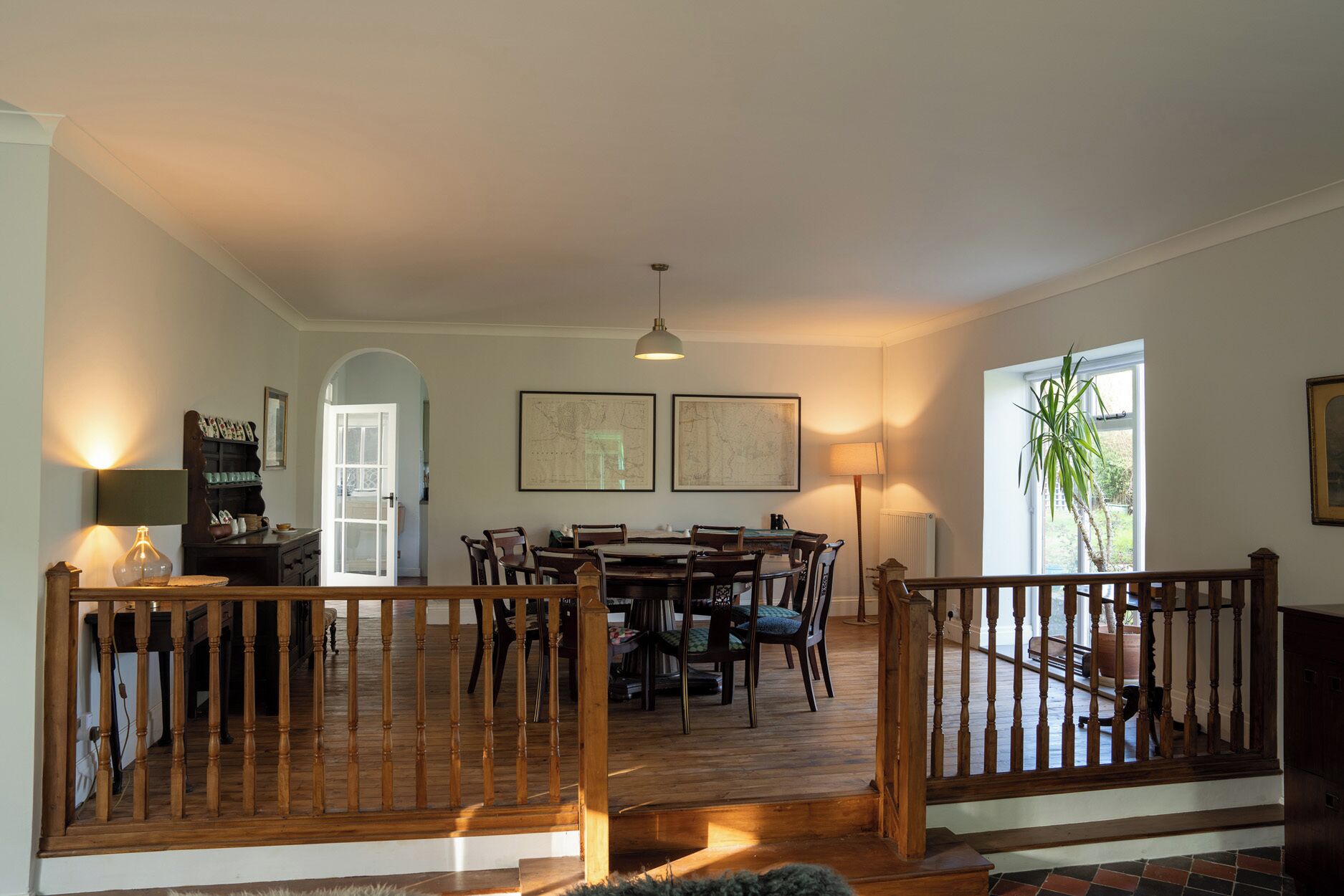 A spacious dining area with a wooden table and chairs, a staircase with a wooden railing, and a large window with a view of the outdoors.